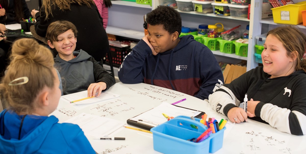 Elementary school students sitting at a table together and socializing while completing math problems